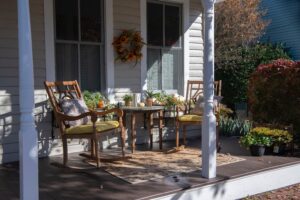 front porch newly painted white and green with 2 wooden cushioned chairs and a fall wreath hung above them